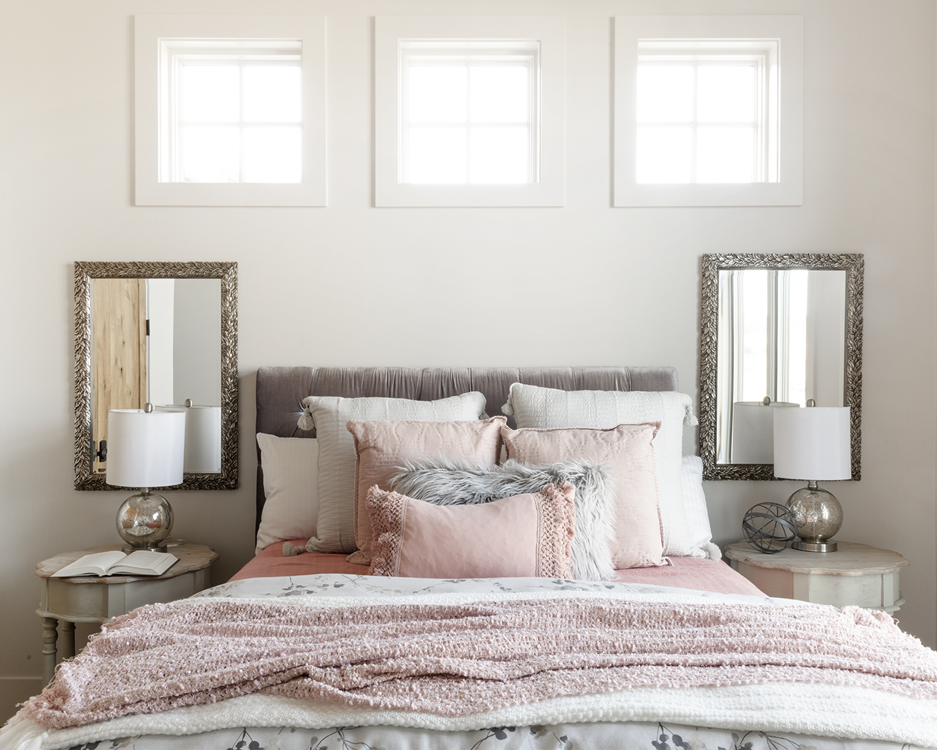 A bedroom with pink and gray bedding and two mirrors.