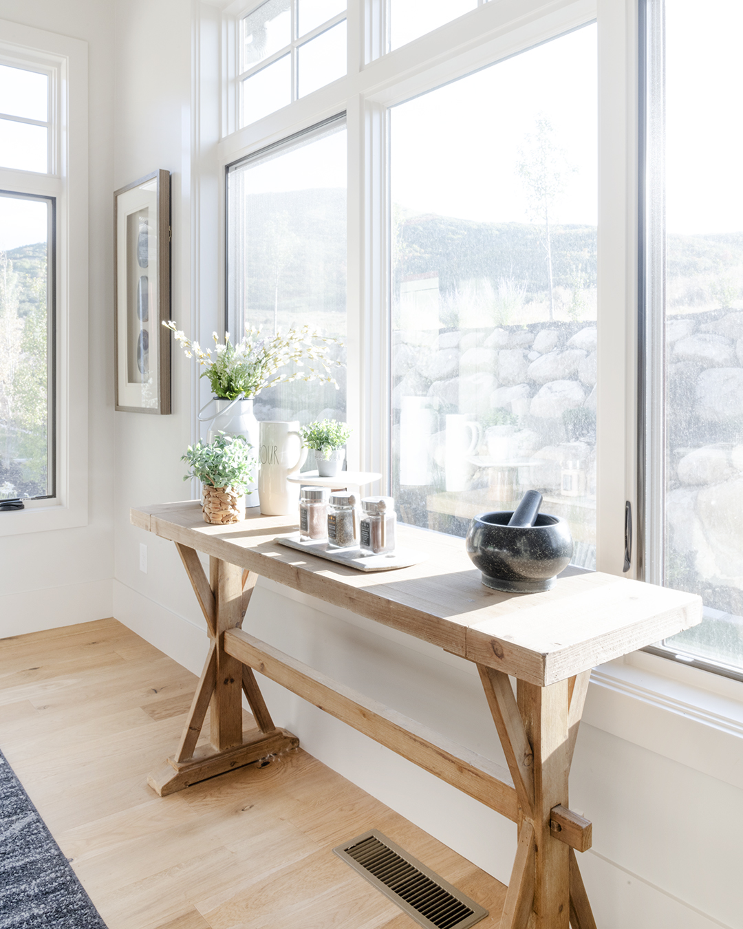 A wooden table with a vase on it in front of a window.