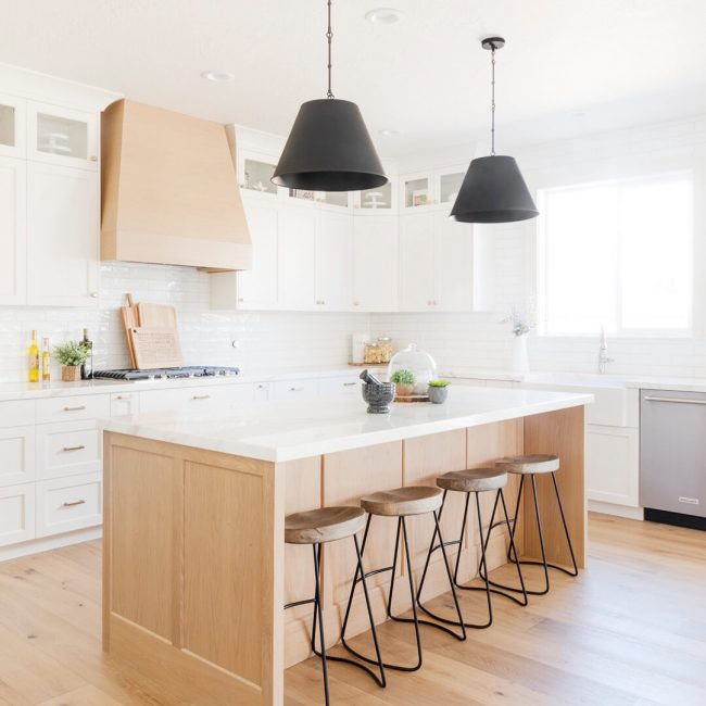 Modern kitchen with wooden floors and black pendant lights.