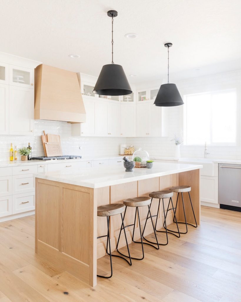 Modern kitchen with wooden floors and black pendant lights.