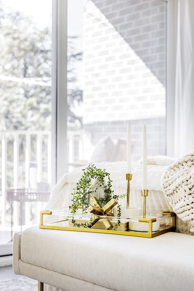 White couch with gold tray on it, accented with green decor.