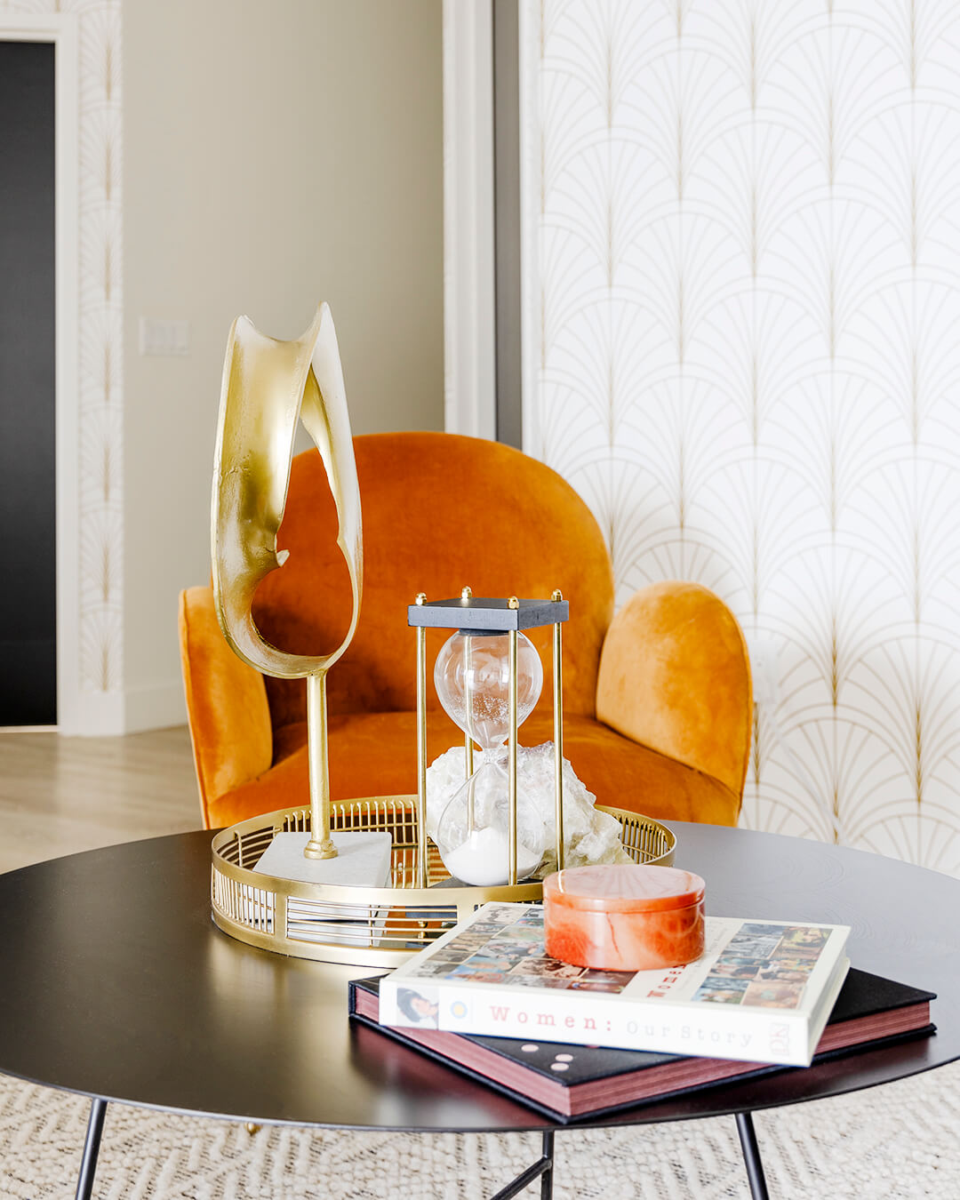 Coffee table with book, orange chair, and lamp in cozy living room setting.