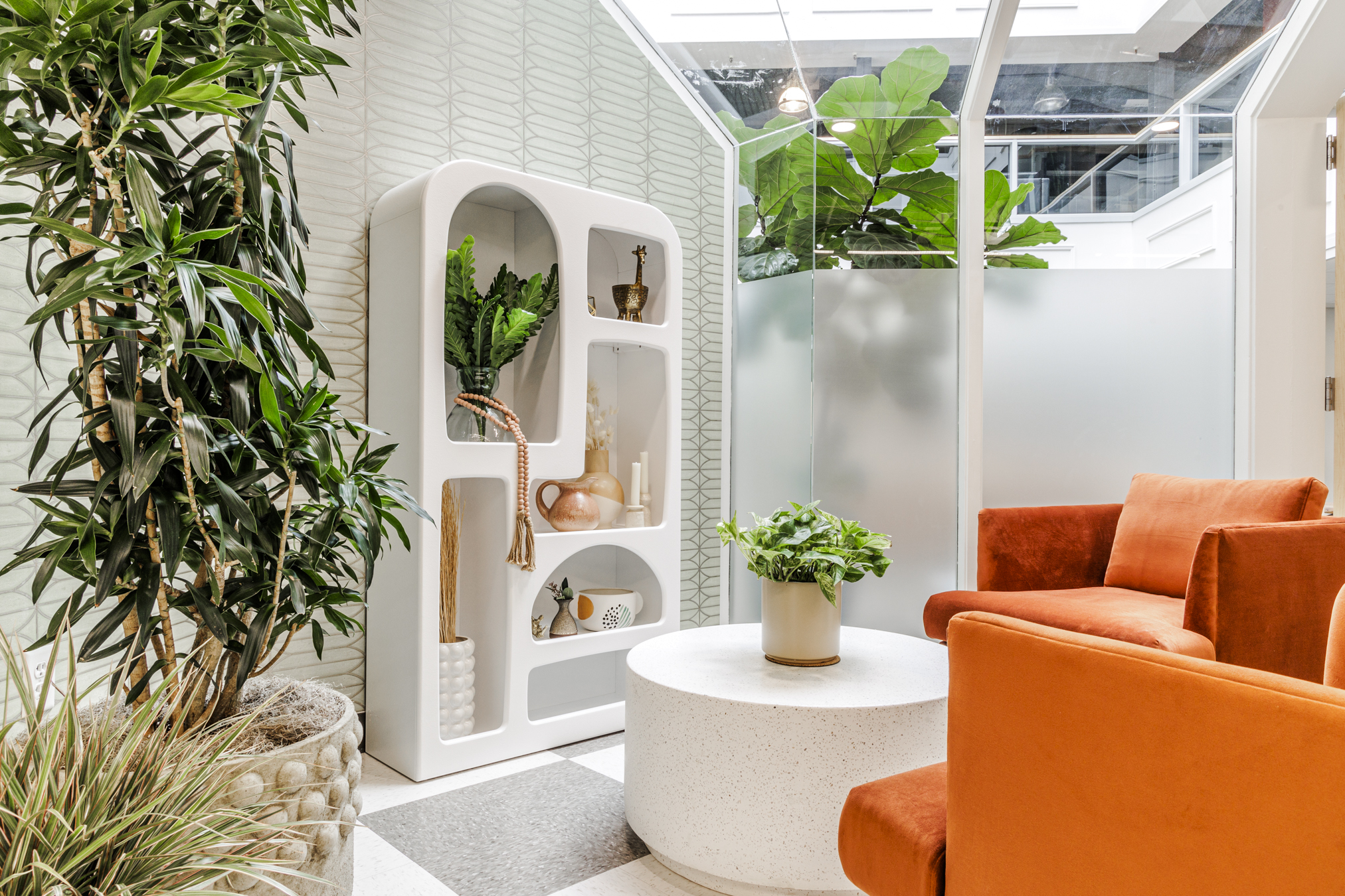 White and orange office with vibrant chairs and green plants.